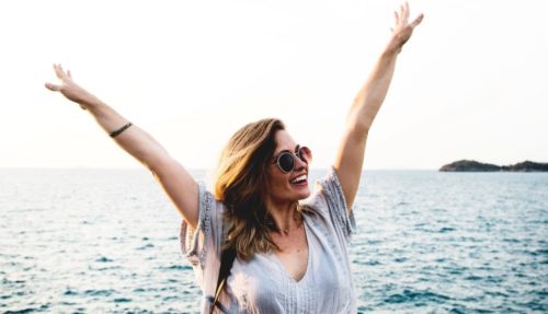 Une femme radieuse portant des lunettes de soleil lèvent ses bras pour signifier son bonheur